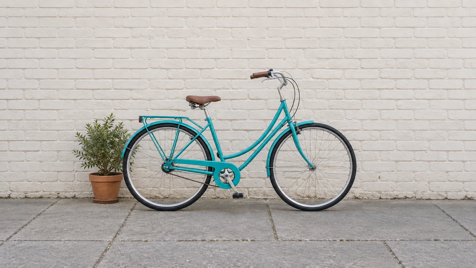 Türkisfarbenes Fahrrad und Pflanztopf vor einer seitlich erweiterten Backsteinwand im Querformat.